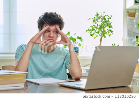 Tired sad young teenage student male sitting at home at desk with laptop computer 118010256