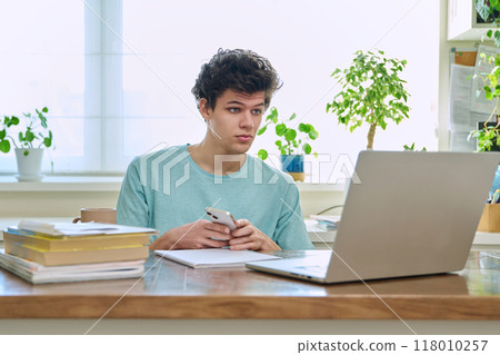 Young guy college student sitting at home at desk using smartphone laptop computer Young guy college student sitting at home at desk using smartphone laptop computer 118010257