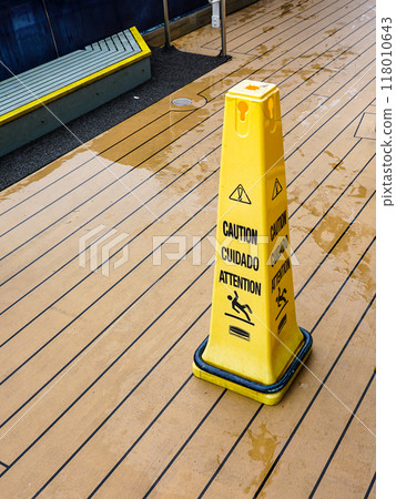 A yellow plastic warning pylon about the slippery wet floor on the deck of a cruise ship A yellow plastic warning pylon about the slippery wet floor on the deck of a cruise ship 118010643