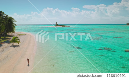 Woman strolling on a beautiful beach with turquoise water and palm trees, a perfect tropical paradise for a relaxing vacation 118010691