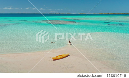 Woman is wading in the shallow, crystal clear turquoise water of a tropical island beach, with a yellow kayak pulled up on the white sand 118010746