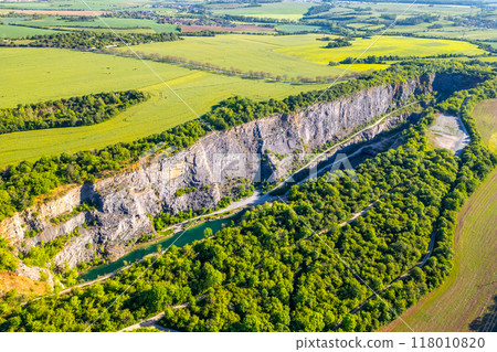 A tranquil morning unfolds over Velka Amerika Quarry, showcasing the impressive rocky cliffs surrounded by lush greenery A tranquil morning unfolds over Velka Amerika Quarry, showcasing the impressive rocky cliffs surrounded by lush greenery 118010820