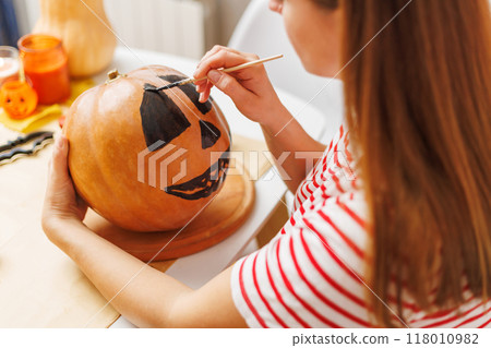 Woman painting face on pumpkin for Halloween Woman painting face on pumpkin for Halloween 118010982