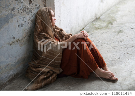A girl in poor clothes sits on the ground A girl in poor clothes sits on the ground 118011454