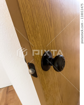 A detailed close-up image of a newly installed black door handle and latch on a wooden door. The door is slightly ajar, revealing the smooth wooden surface and the latch mechanism. The background 118011475