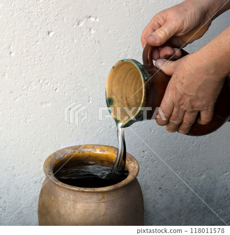 A hand holds a clay jar and pours water 118011578