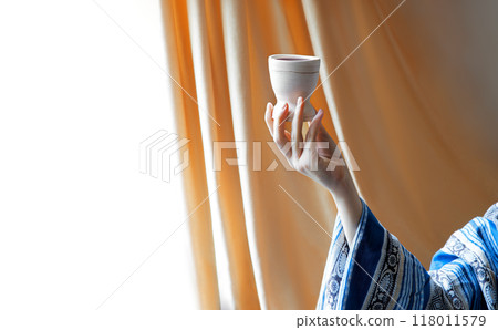 A hand in ancient clothing holds a clay bowl A hand in ancient clothing holds a clay bowl 118011579