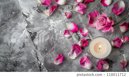 Delicate pink rose with petals surrounding a lit candle on a textured gray surface Delicate pink rose with petals surrounding a lit candle on a textured gray surface 118011712