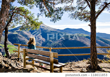 Curly-haired blonde woman, sitting on a bench, looking at the fantastic views of the Ribes mountains, in the Ripolles region, Girona Curly-haired blonde woman, sitting on a bench, looking at the fantastic views of the Ribes mountains, in the Ripolles region, Girona 118011853