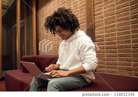 Wavy haired male student in library hall working on laptop Wavy haired male student in library hall working on laptop 118012195