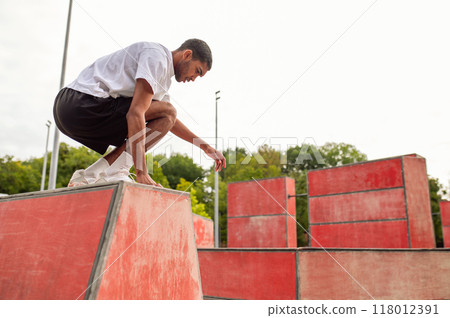 Young tall sportsman leaping over the brick and looking concentrated Young tall sportsman leaping over the brick and looking concentrated 118012391