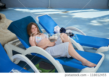 Relaxing Summer Vacation: Teenage Girl Lounging on Sunbed in Mediterranean Paradise with Palm Trees and Blue Sky. Idyllic Mediterranean Getaway: Young Girl Sunbathing on Sunbed Amidst Palm Trees 118012455