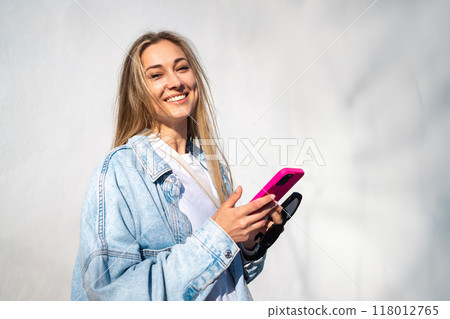 Happy woman holding smartphone against wall Happy woman holding smartphone against wall 118012765