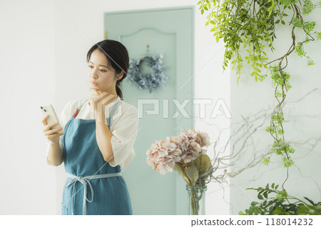 A woman in an apron looking at her smartphone A woman in an apron looking at her smartphone 118014232