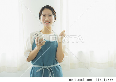 A woman in an apron looking at her smartphone A woman in an apron looking at her smartphone 118014336