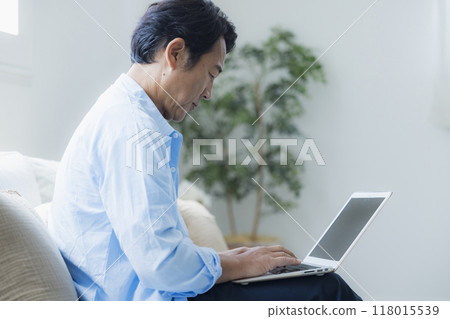 Middle-aged man using a laptop in the living room Middle-aged man using a laptop in the living room 118015539