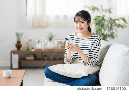 一名年輕女子在沙發上使用智慧型手機。 118016100