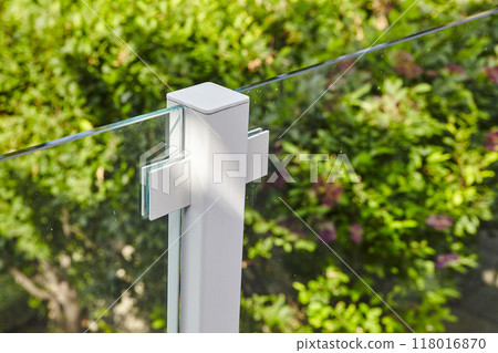 Modern Glass Balustrade Detail with Metal Clamps and Greenery Background 118016870