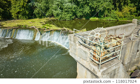Rusty wheel Maumee River Dam with logs and algae growth above waterfall with green trees Fort Wayne, IN aerial Rusty wheel Maumee River Dam with logs and algae growth above waterfall with green trees Fort Wayne, IN aerial 118017024