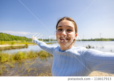 Joyful Young Woman Embracing Nature and Enjoying Life by the Beautiful Water Body 118017913