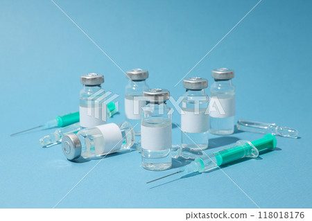 Glass medical bottles and ampoules with vaccine and syringes on blue background 118018176