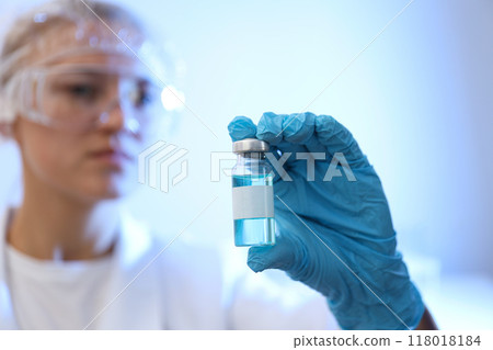 Glass bottle with vaccine in doctor's gloved hand on blue background, close up 118018184