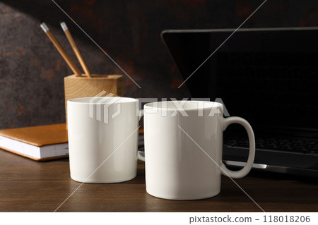 White cups on a wooden table with a laptop White cups on a wooden table with a laptop 118018206
