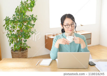 A middle-aged woman working on a computer with a cup of coffee in hand 118018245
