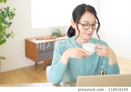 A middle-aged woman working on a computer with a cup of coffee in hand A middle-aged woman working on a computer with a cup of coffee in hand 118018249