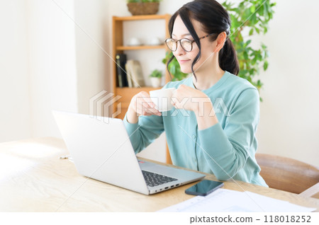 A middle-aged woman working on a computer with a cup of coffee in hand A middle-aged woman working on a computer with a cup of coffee in hand 118018252