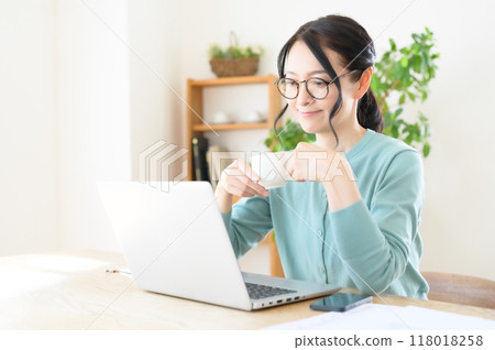A middle-aged woman working on a computer with a cup of coffee in hand A middle-aged woman working on a computer with a cup of coffee in hand 118018258
