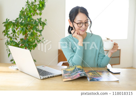 Middle-aged woman looking at a pamphlet at a table Middle-aged woman looking at a pamphlet at a table 118018315