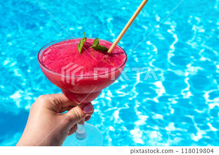 Hand with chilled raspberry Daiquiri with mint in hand by pool on sunny day. Concept of summer fun and refreshing drinks Hand with chilled raspberry Daiquiri with mint in hand by pool on sunny day. Concept of summer fun and refreshing drinks 118019804