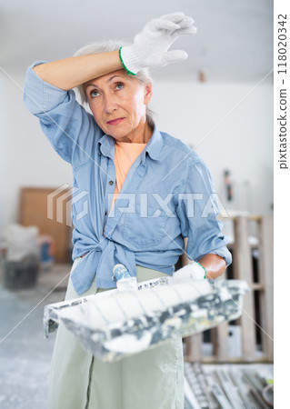 Portrait of an elderly tired female house painter in renovated room Portrait of an elderly tired female house painter in renovated room 118020342