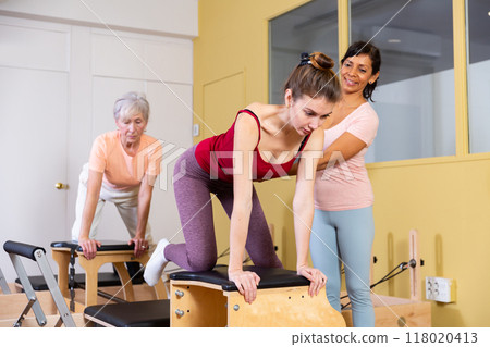 Young woman performs an exercise on a combined chair with instructor 118020413