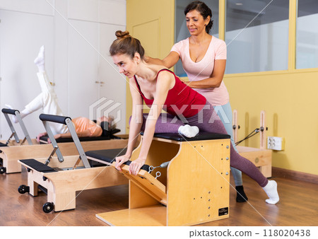 Young woman performs an exercise on a combined chair with instructor 118020438