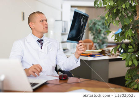 Male physician sitting in office and looking at roentgenogram 118020523