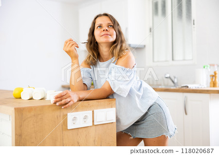 Young woman eating tasty yogurt in kitchen Young woman eating tasty yogurt in kitchen 118020687
