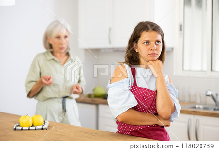 Upset girl at home kitchen while worried elderly mother reprimanding her. Family conflicts concept 118020739