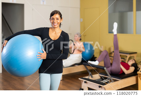 Hispanic woman standing with gym ball in pilates studio 118020775