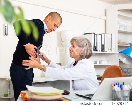 Man complaining about stomach ache to mature woman physician 118020815