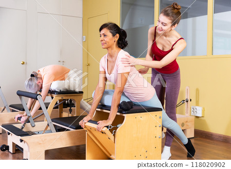 Hispanic woman practicing pilates on wunda chair with young trainer 118020902