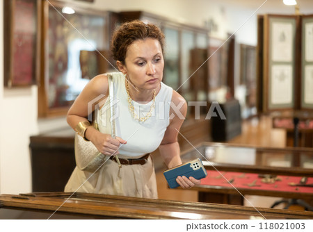 Visiting historical museum - woman carefully examines antique exhibits 118021003