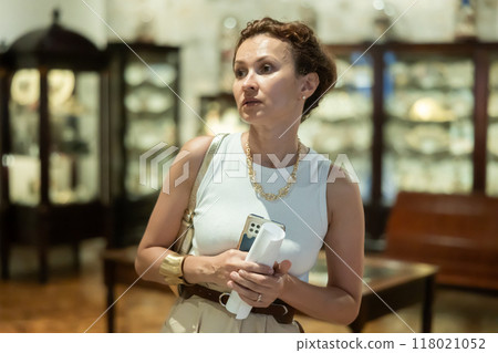 Woman curiously observing antique artifacts in historical museum 118021052