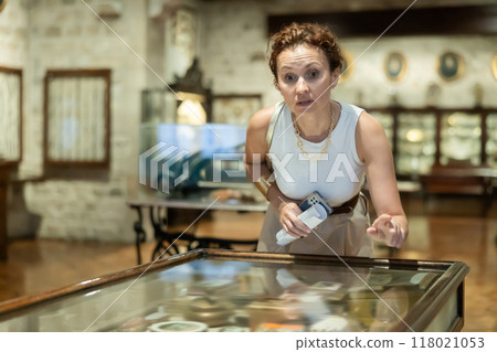 Woman inspecting items displayed in glass showcase at museum 118021053