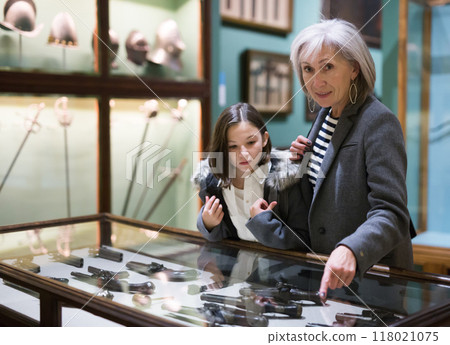Preteen girl with grandmother viewing ancient handguns in museum 118021075