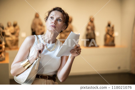Interested woman reading guide while exploring museum exhibit 118021076