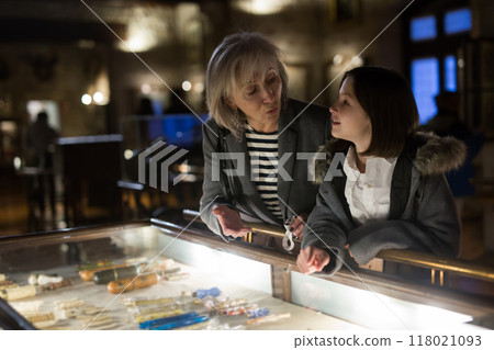 Aged female tutor with preteen girl exploring showpieces in museum Aged female tutor with preteen girl exploring showpieces in museum 118021093