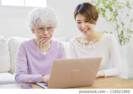 Daughter teaching her mother how to use a laptop in the living room Daughter teaching her mother how to use a laptop in the living room 118021860