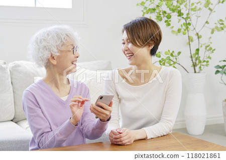 Mother and daughter using smartphone in living room Mother and daughter using smartphone in living room 118021861
